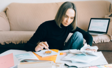 a woman in a black turtleneck and jeans doing her taxes at a coffee table while sitting in front of a brown couch
