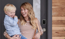 woman holding small child next to a smart lock outside their front door