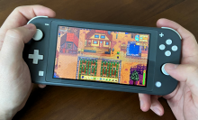 a close-up of a man's hands playing "stardew valley" on a gray nintendo switch lite