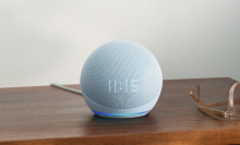 The 5th generation Echo Dot with clock resting on a table next to a pair of glasses