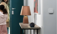 The Amazon Echo Dot resting on a table next to a lamp while a mother and daughter exit their house.