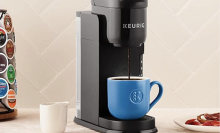 The Keurig K-Express Coffee Maker sitting on a countertop while making a cup of coffee, surrounded by a rack of K-Cup pods.