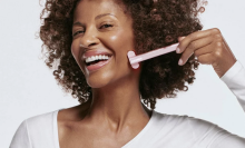 Curly-haired woman holding up the Solawave Skincare Wand to her face while smiling.