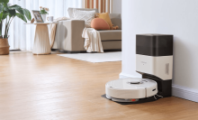 White Roborock vacuum and dock sitting against wall with living room furniture in background