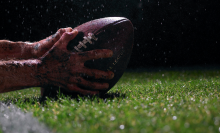 close up of hands catching a football on field with rain
