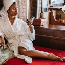 Black woman sitting in a robe looking at her phone 