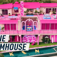 Drone aerial shot of the pink Barbie Dreamhouse, gold balloon letters spelling KEN float in the swimming pool.