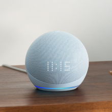 The 5th generation Echo Dot with clock resting on a table next to a pair of glasses