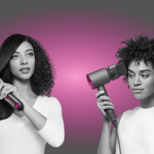 Two people styling hair with Dyson hair tools with gray and pink graphic in background