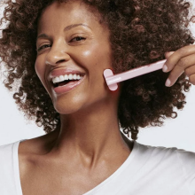 Curly-haired woman holding up the Solawave Skincare Wand to her face while smiling.