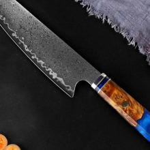 The Seido Kiritsuke Damascus Chef Knife laying on a black surface with tomatoes surrounding it.