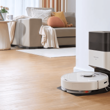 White Roborock vacuum and dock sitting against wall with living room furniture in background