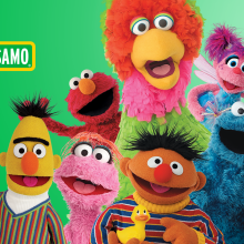 A group of Sesame Street and Plaza Sesamo characters smile to camera. 