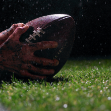 close up of hands catching a football on field with rain