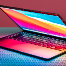 a halfway open m1 apple macbook air sitting on a textured surface in front of a pink and aqua background