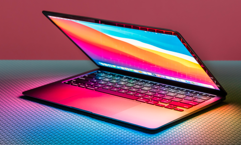 a halfway open m1 apple macbook air sitting on a textured surface in front of a pink and aqua background