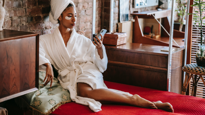 Black woman sitting in a robe looking at her phone 