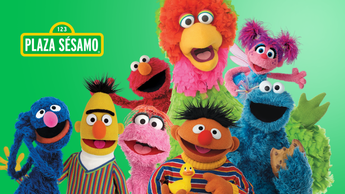 A group of Sesame Street and Plaza Sesamo characters smile to camera. 